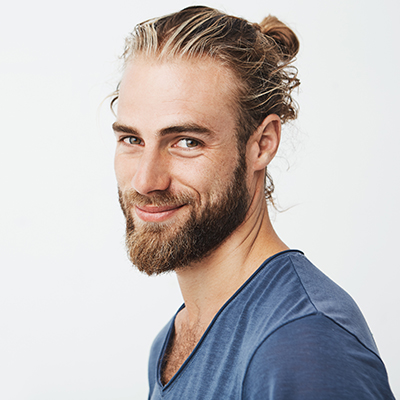 Close up portrait of handsome manly guy with beard posing in three quarters, looking in camera and happily smiling