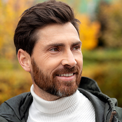 Mature bearded man smiling outdoors while looking away
